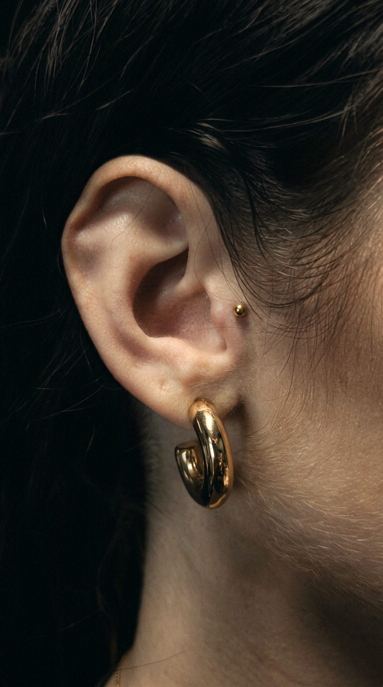 Ohr mit goldenem Creolen-Schmuck und Tragus-Piercing im Detail